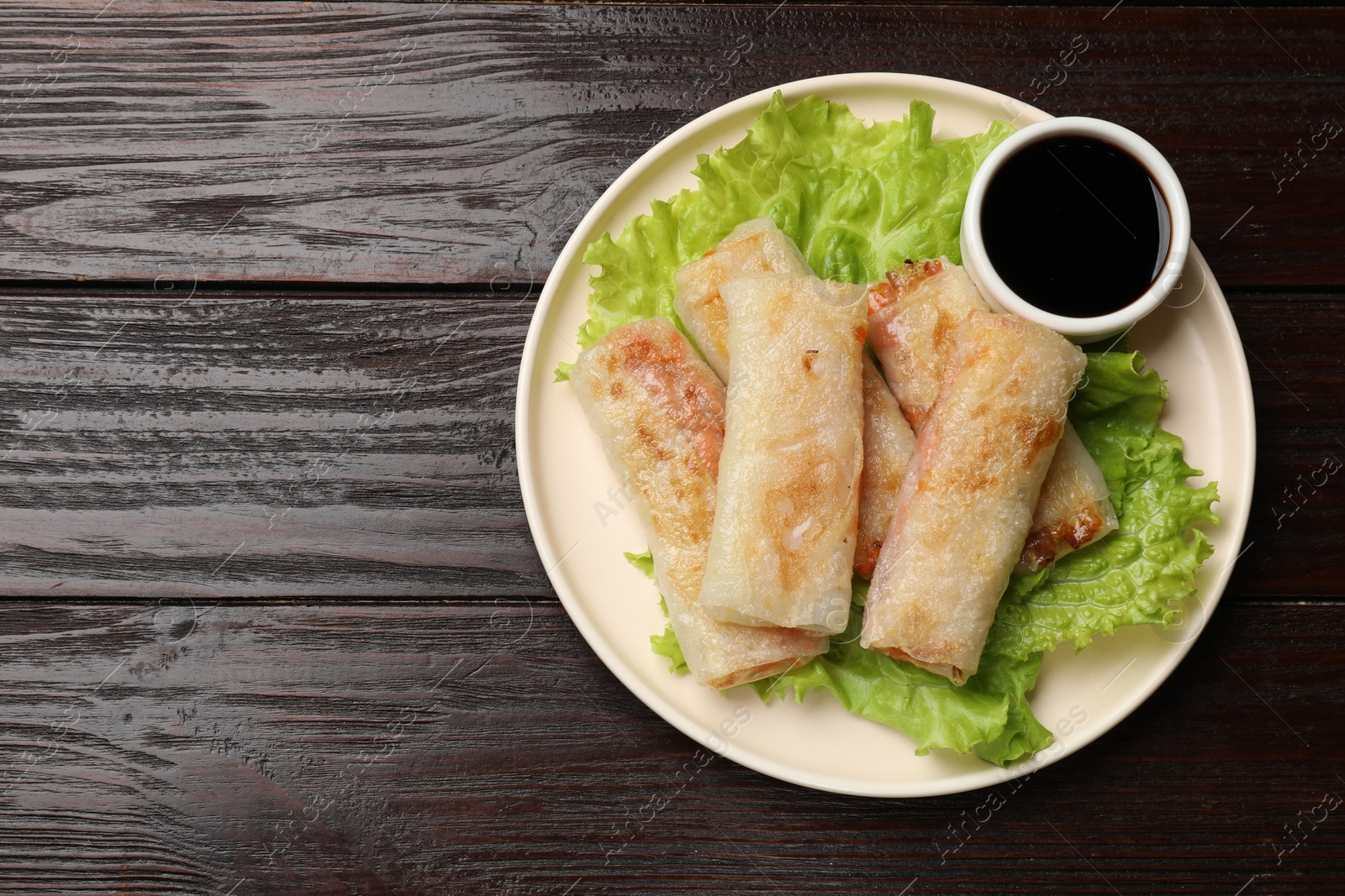 Photo of Delicious fried spring rolls with soy sauce on wooden table, top view. Space for text