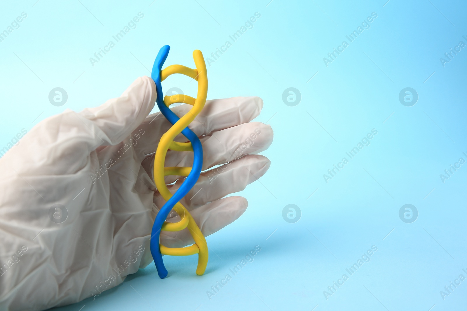 Photo of Scientist with DNA molecule model made of plasticine on light blue background, closeup. Space for text