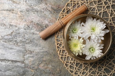 Photo of Tibetan singing bowl with water, beautiful chrysanthemum flowers and mallet on table, top view. Space for text