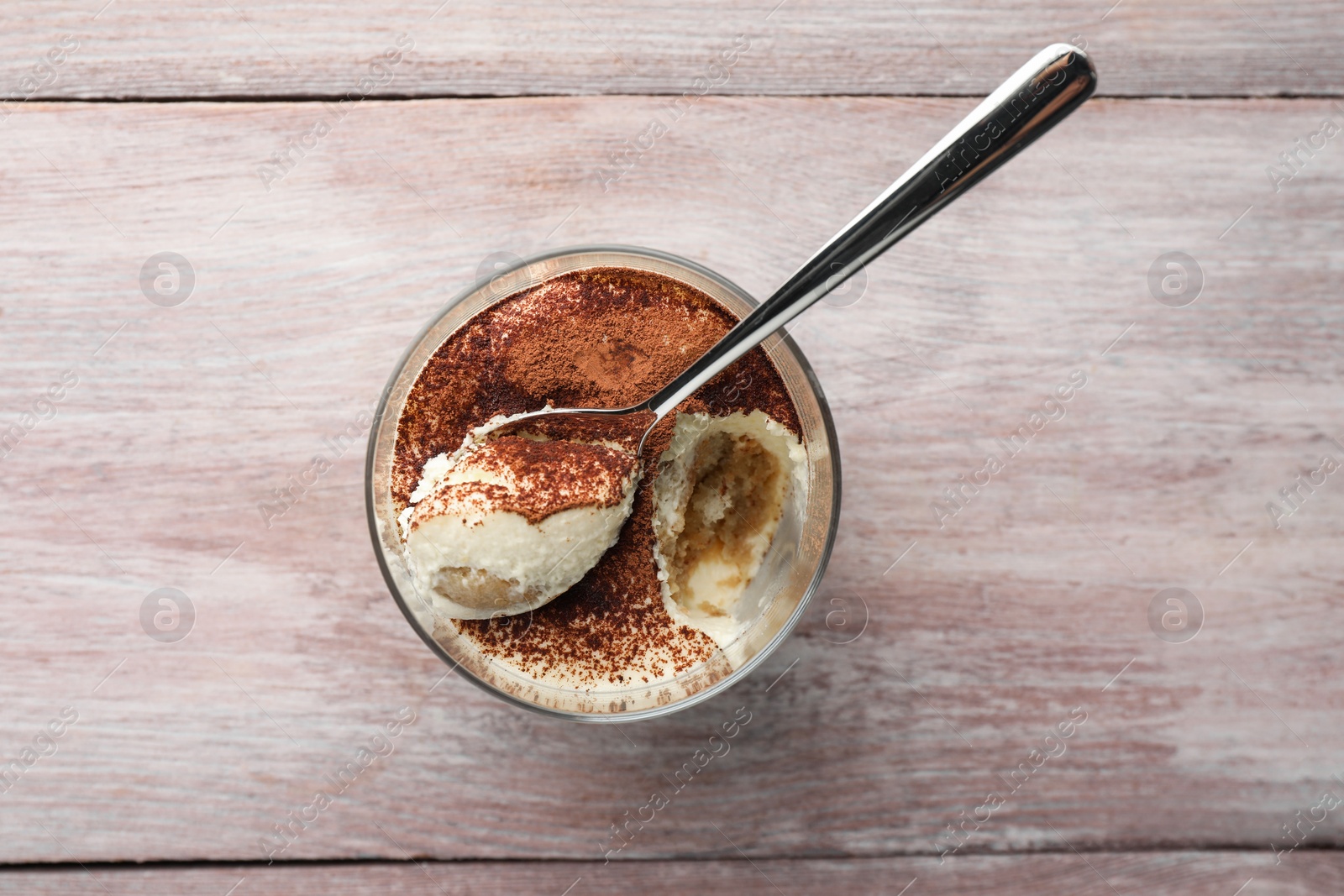 Photo of Delicious tiramisu in glass and spoon on wooden table, top view