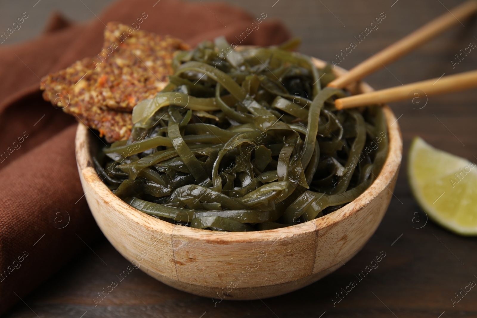 Photo of Tasty seaweed salad in bowl served on wooden table, closeup