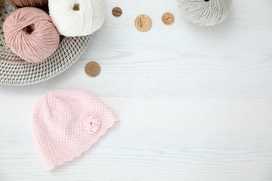 Flat lay composition with crocheted hat and supplies on white wooden table, space for text. Engaging in hobby