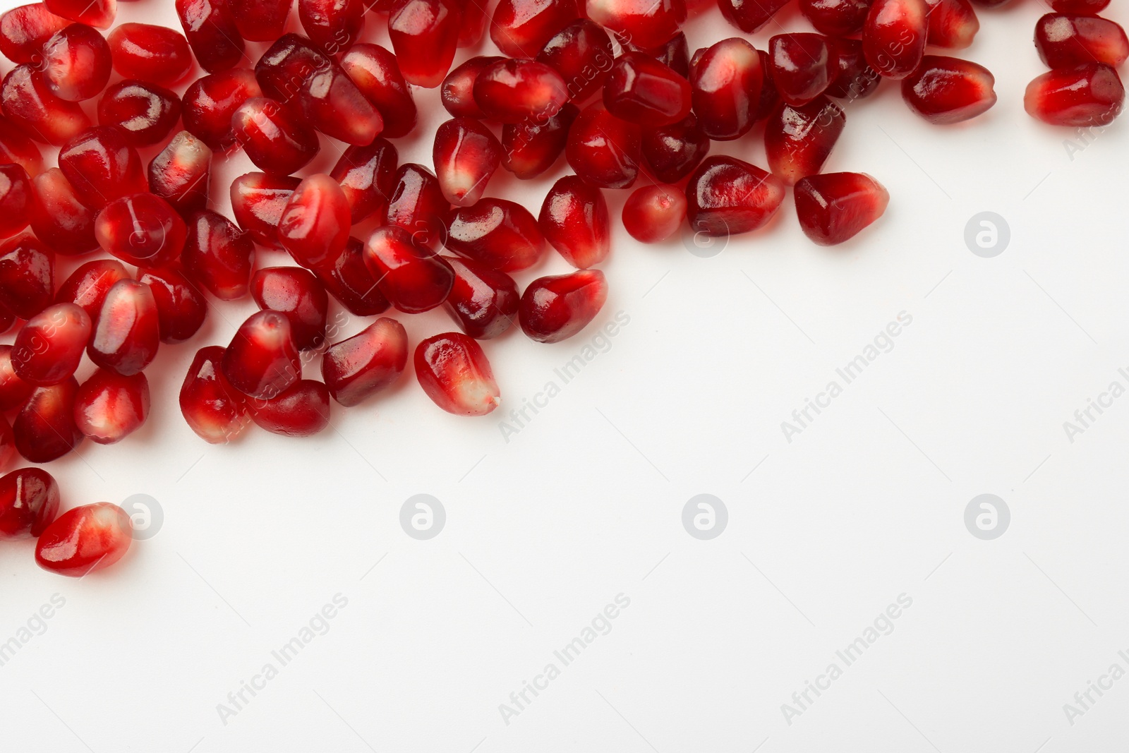 Photo of Many ripe juicy pomegranate grains on white background, flat lay. Space for text