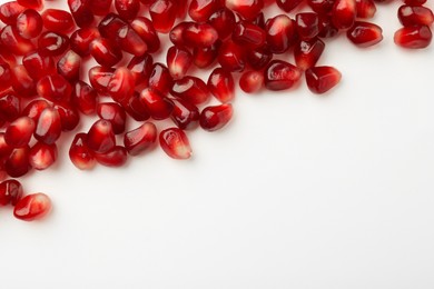 Photo of Many ripe juicy pomegranate grains on white background, flat lay. Space for text