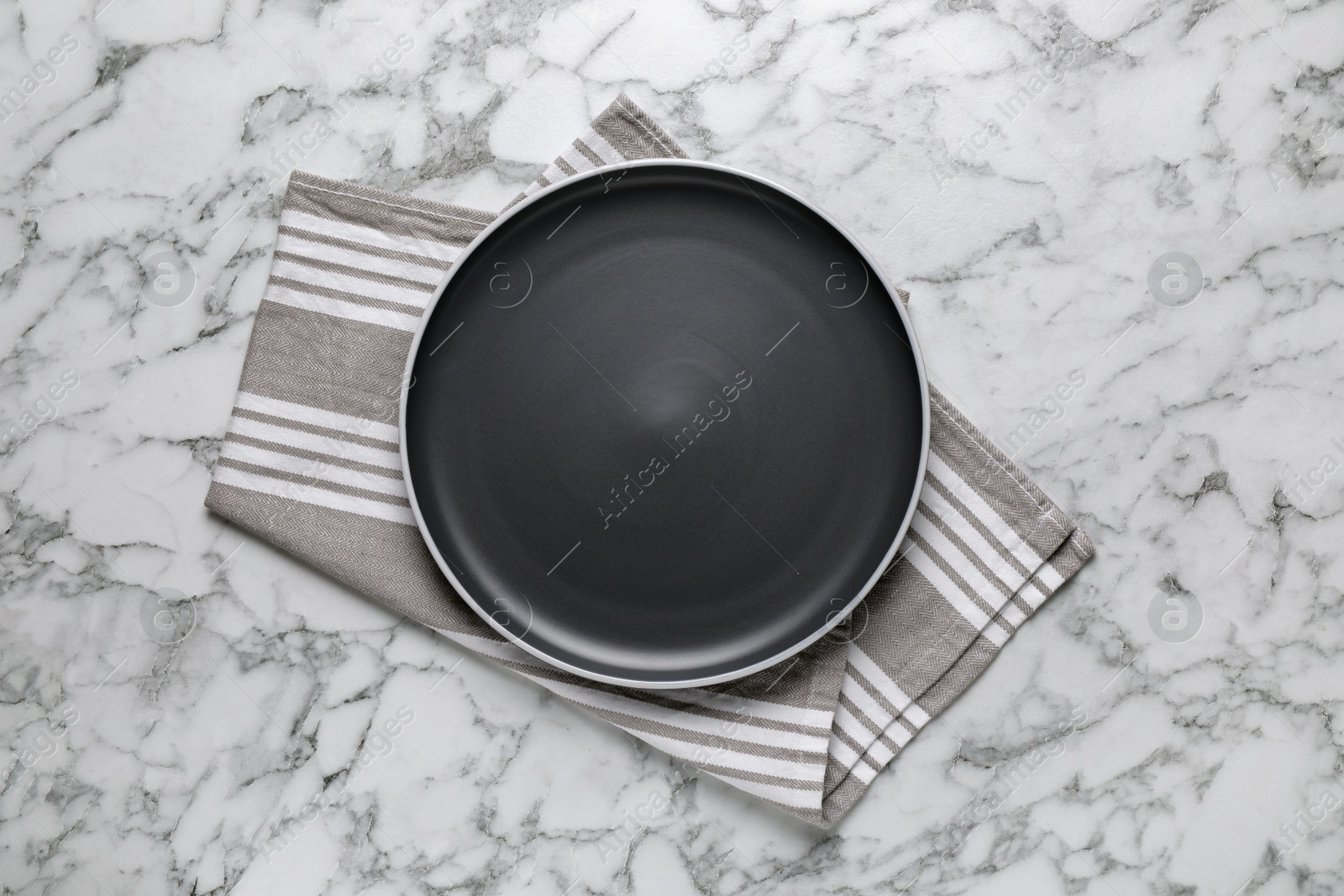 Photo of New dark plate and napkin on white marble table, top view