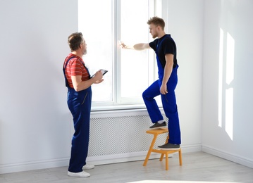 Service men measuring window for installation indoors