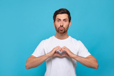 Handsome man making heart with hands and blowing kiss on light blue background