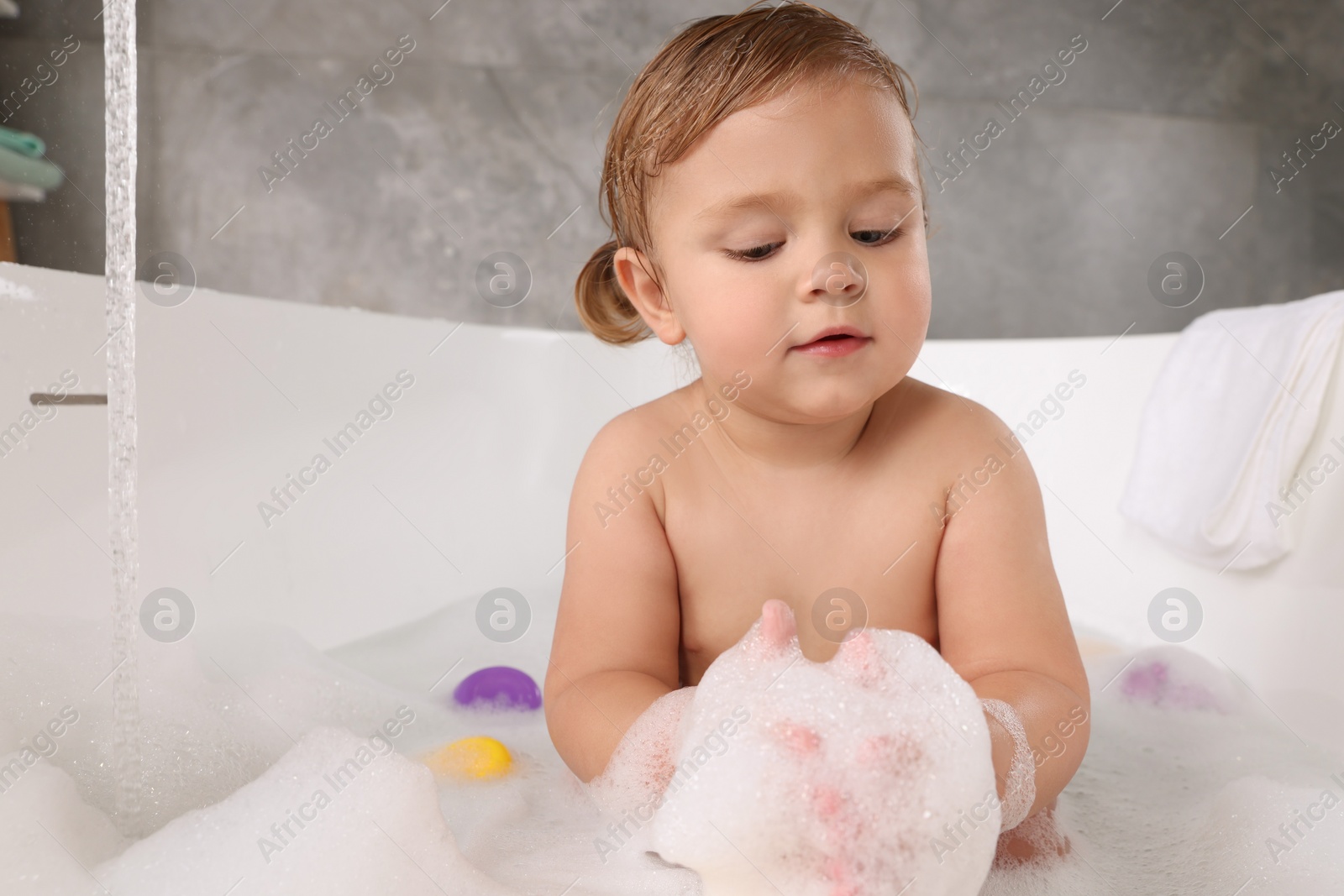 Photo of Cute little girl taking bubble bath with toys indoors