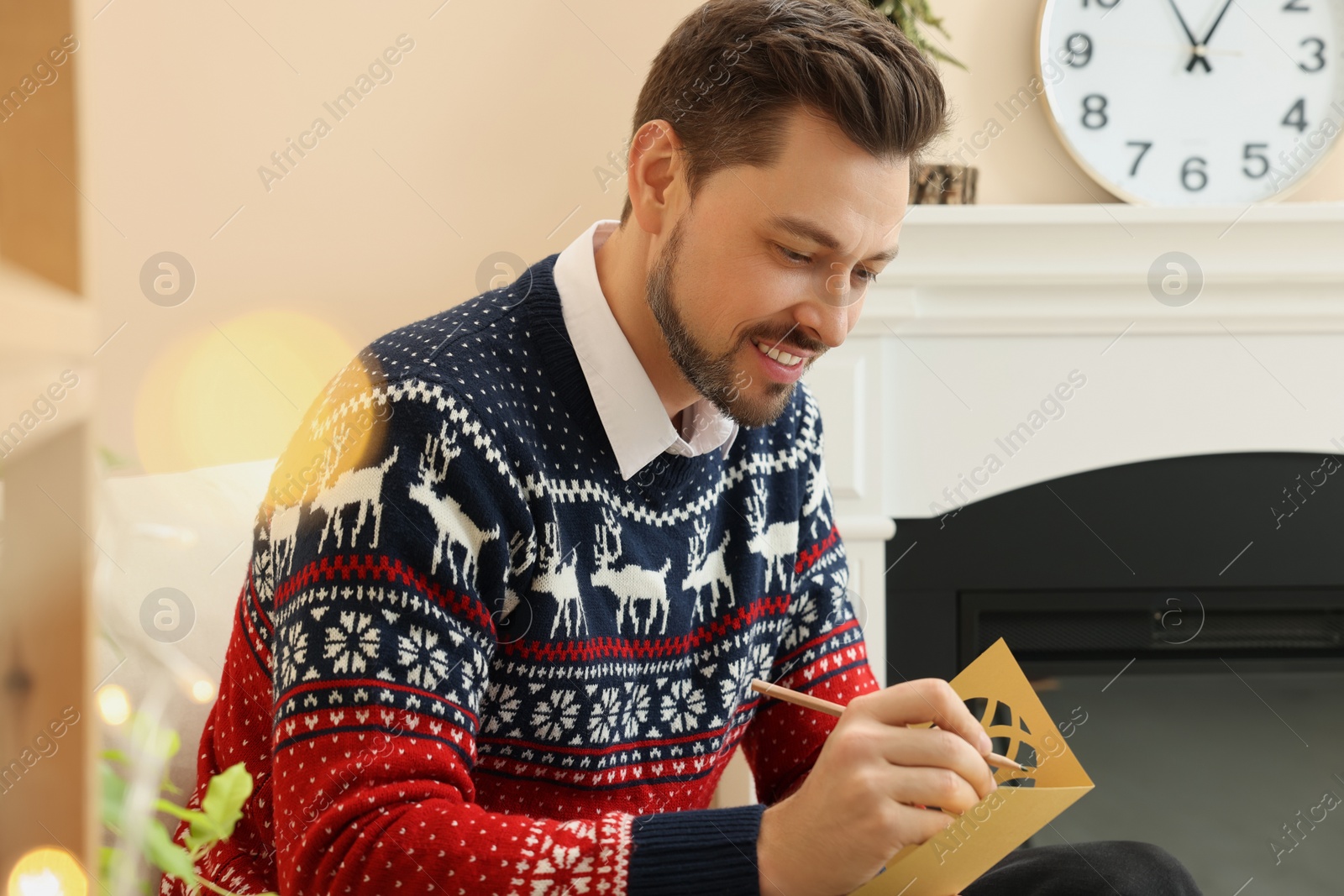 Photo of Happy man writing wishes in Christmas greeting card in living room