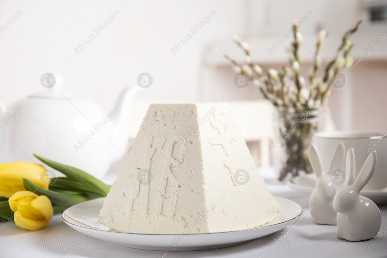 Photo of Traditional cottage cheese Easter paskha, decorative bunnies and yellow tulips on white fabric