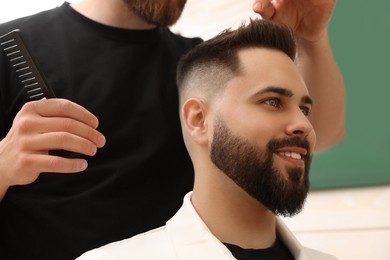 Photo of Professional hairdresser working with client in barbershop, closeup