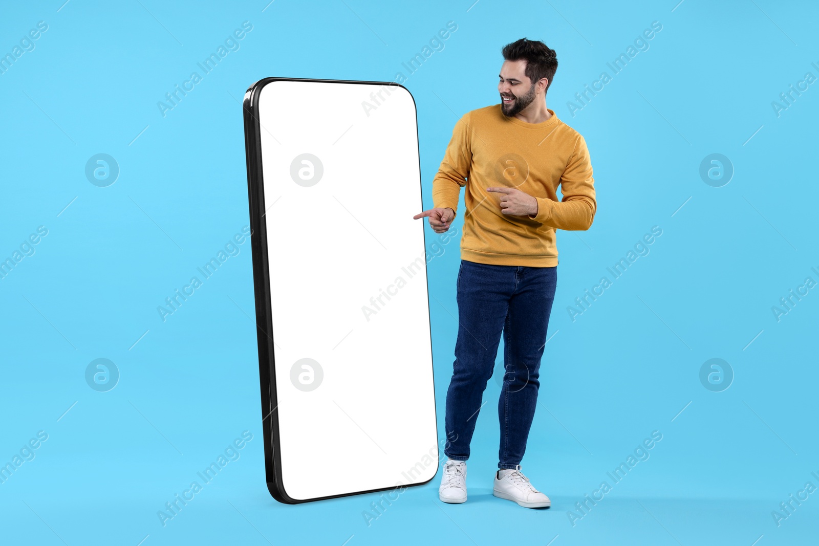 Image of Man pointing at huge mobile phone with empty screen on light blue background. Mockup for design