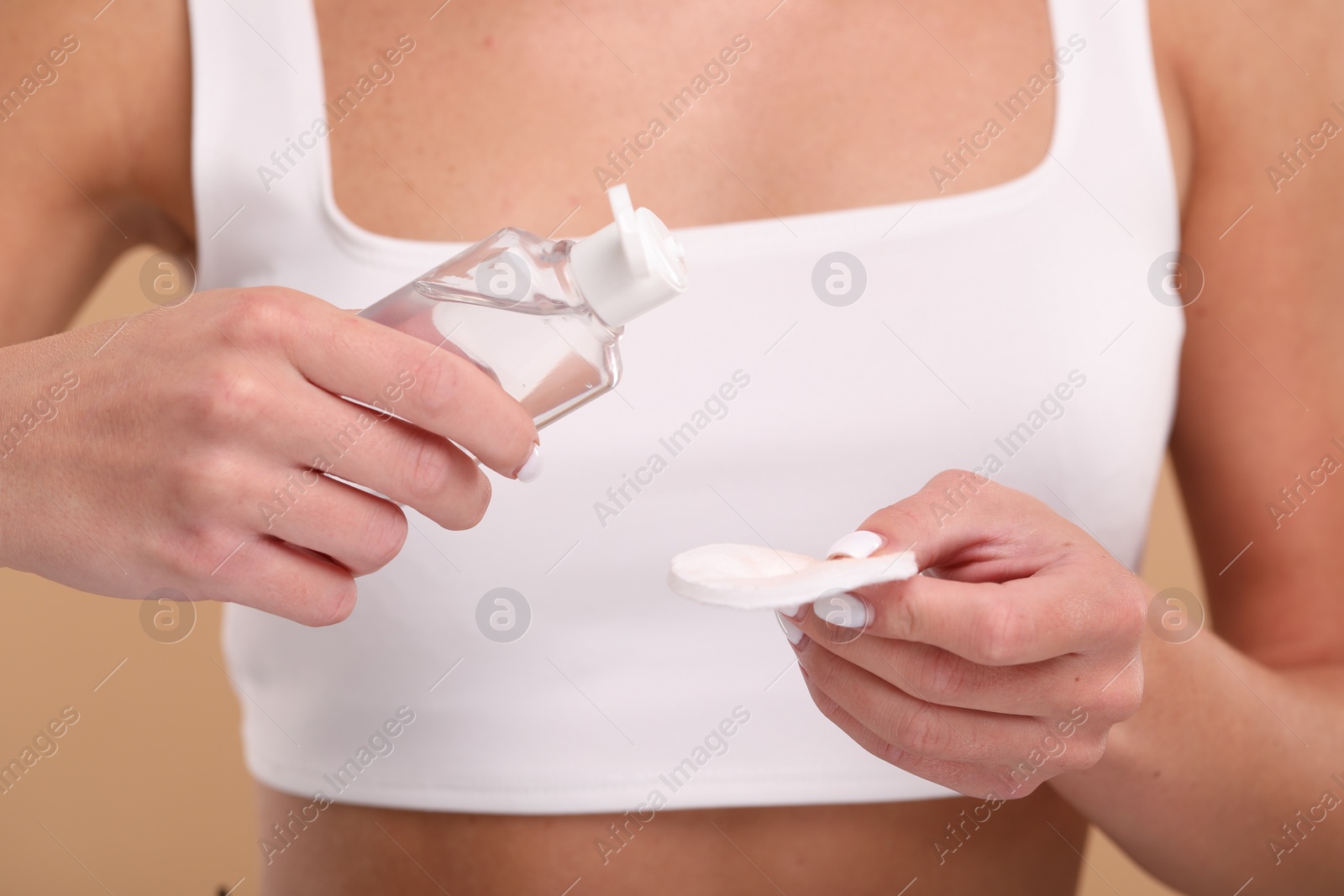 Photo of Woman with makeup remover and cotton pad on beige background, closeup