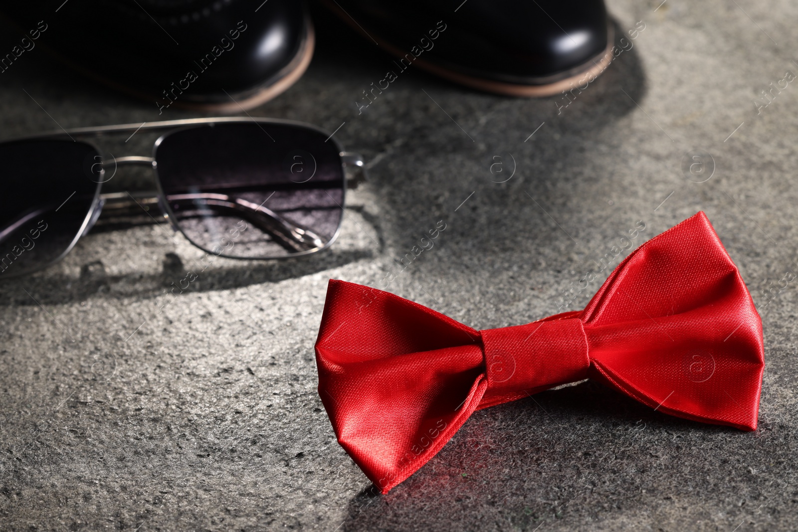 Photo of Stylish red bow tie and sunglasses on gray textured background