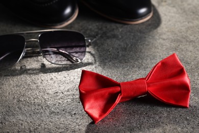Stylish red bow tie and sunglasses on gray textured background