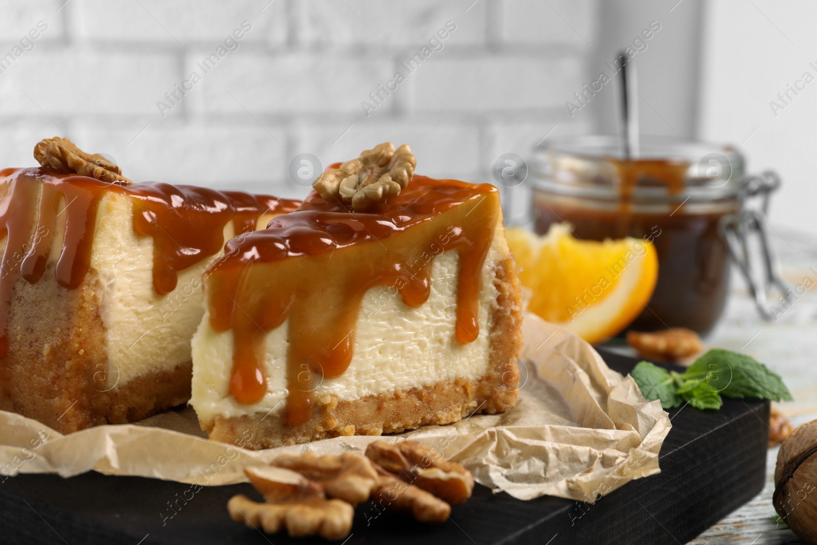 Photo of Pieces of delicious caramel cheesecake with walnuts served on table, closeup