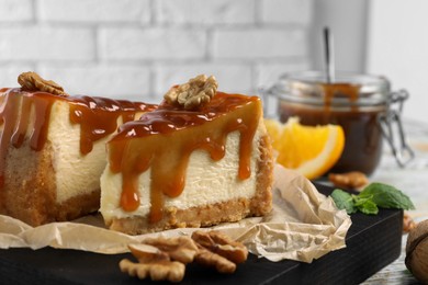 Pieces of delicious caramel cheesecake with walnuts served on table, closeup
