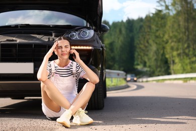 Stressed woman talking on smartphone near broken car outdoors, space for text