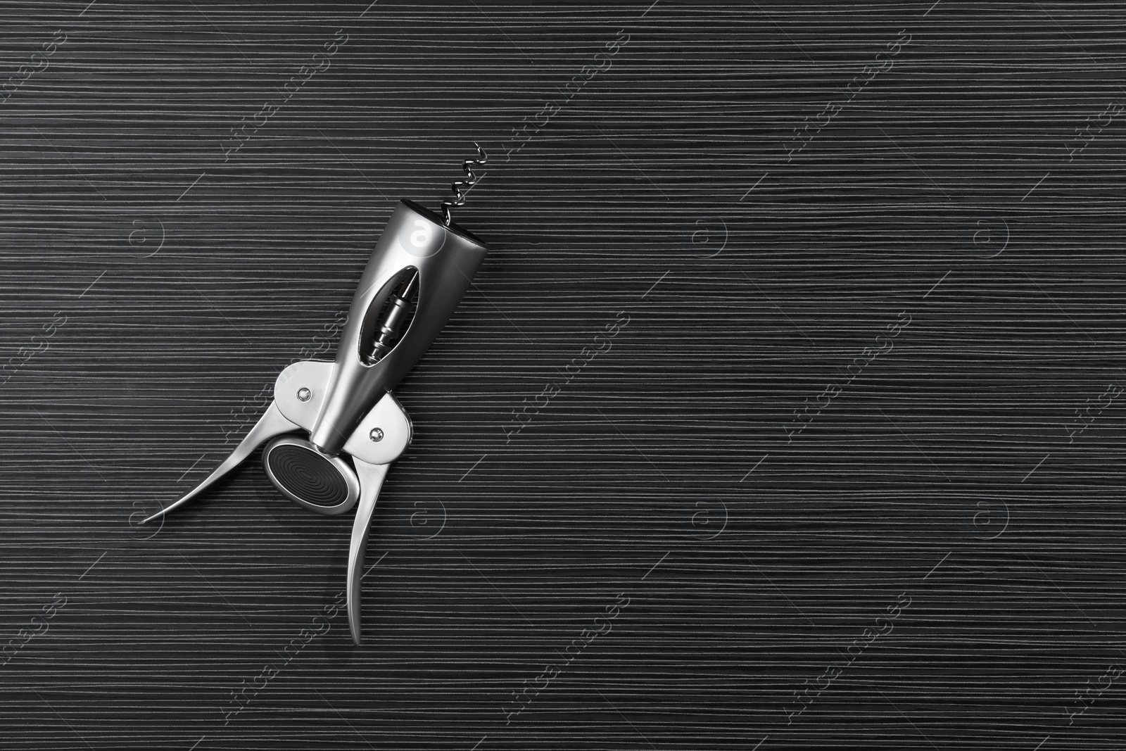 Photo of One wing corkscrew on black wooden table, top view. Space for text