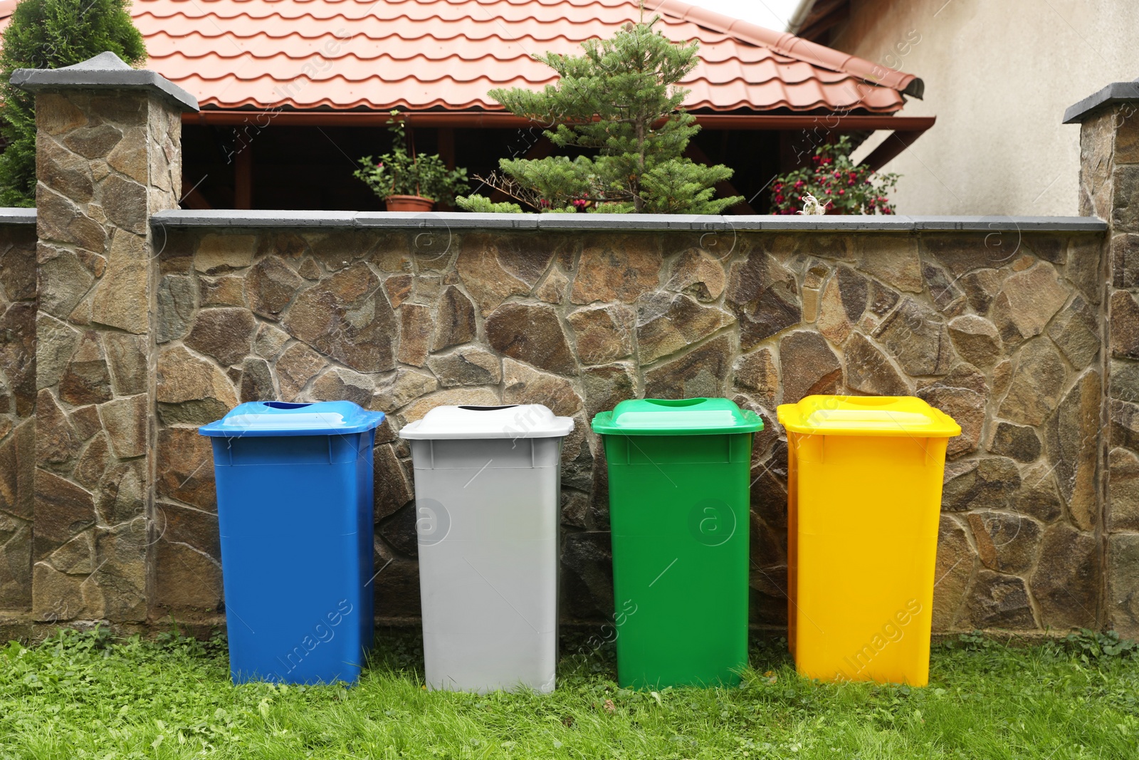 Photo of Many colorful recycling bins near stone fence outdoors