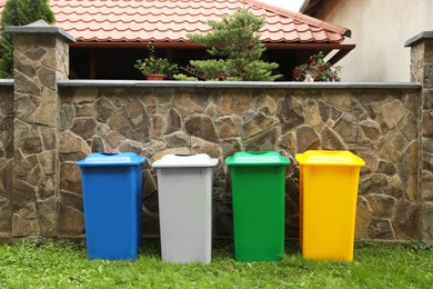 Many colorful recycling bins near stone fence outdoors