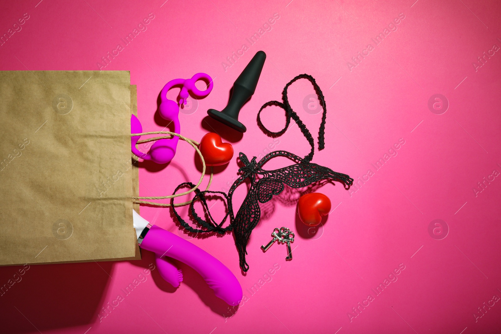 Photo of Paper shopping bag with different sex toys on pink background, flat lay