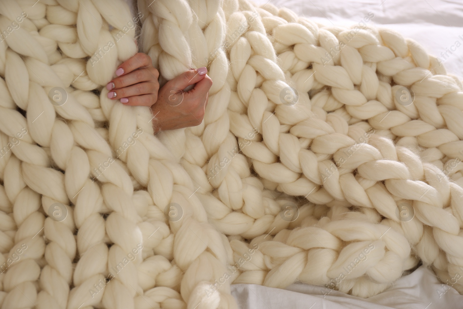 Photo of Woman covered with knitted plaid on bed, closeup