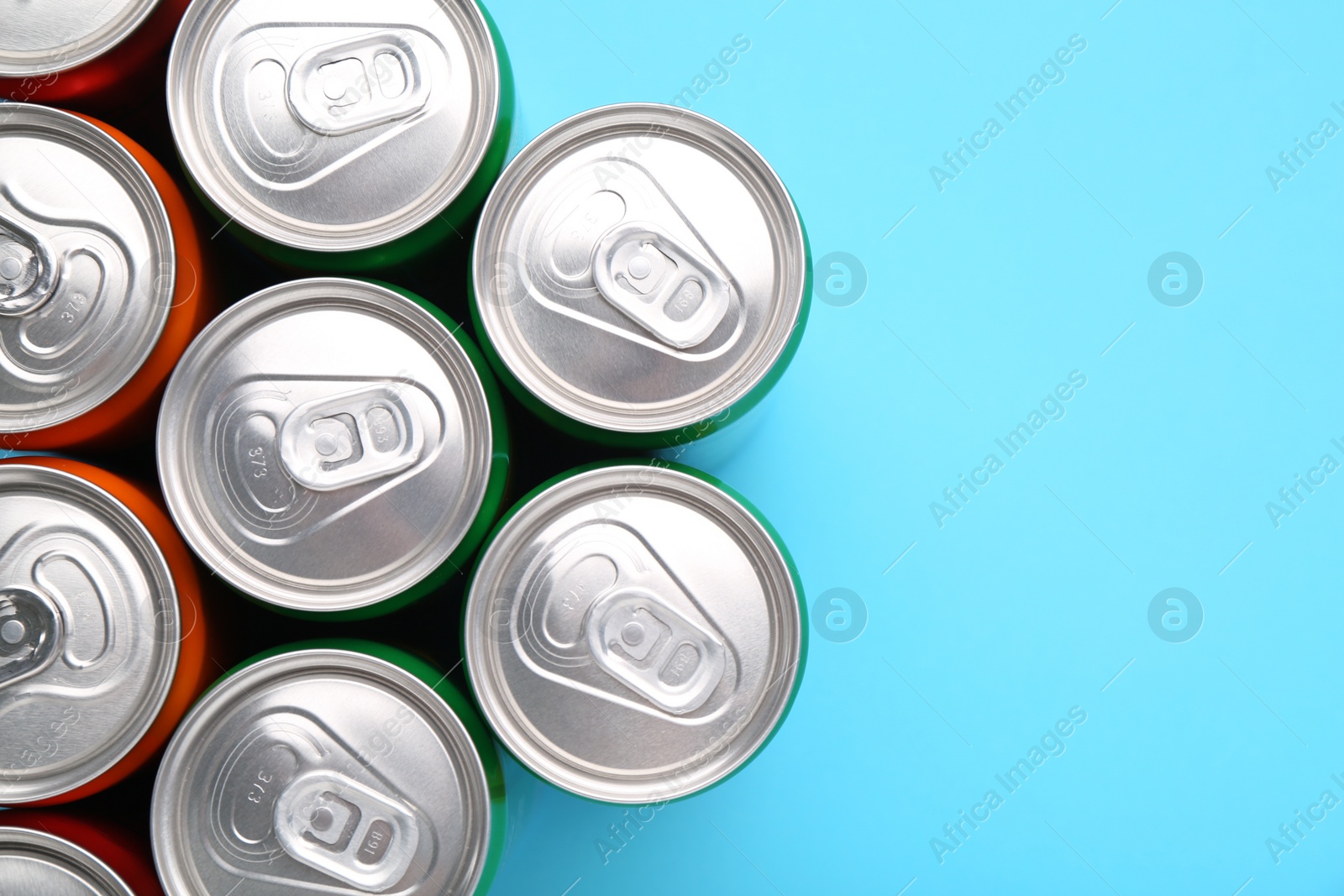 Photo of Energy drink in cans on light blue background, top view. Space for text