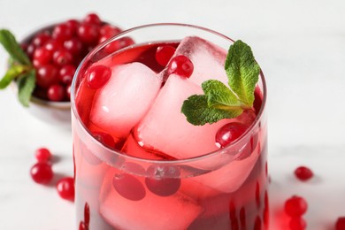Tasty cranberry juice with ice cubes in glass and fresh berries on white wooden table, closeup