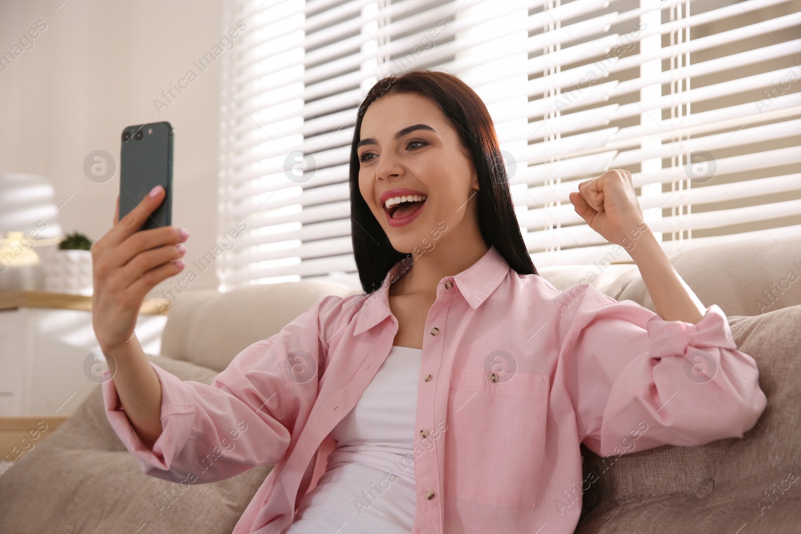 Photo of Emotional woman participating in online auction using smartphone at home