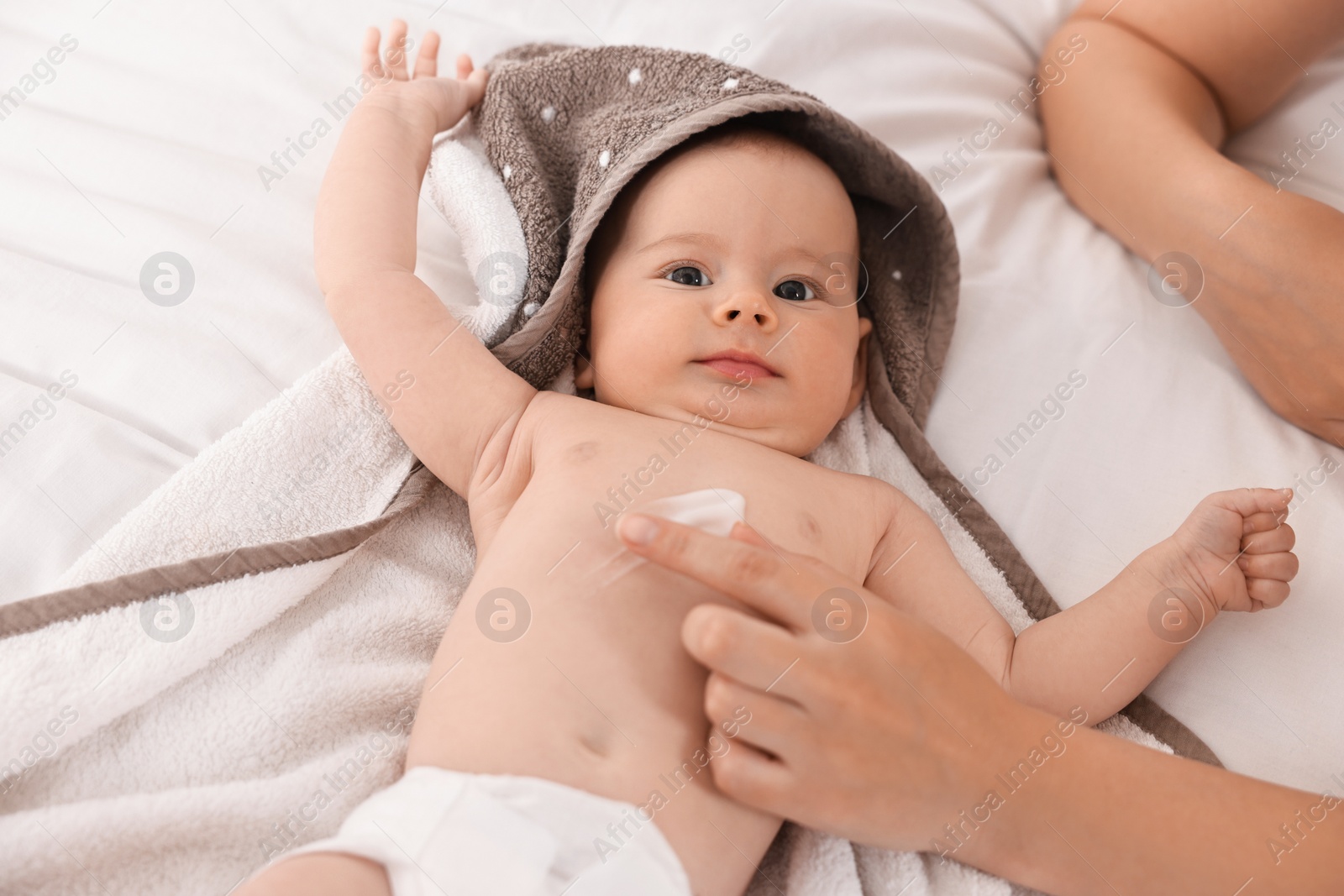 Photo of Woman applying body cream onto baby`s skin on bed, closeup