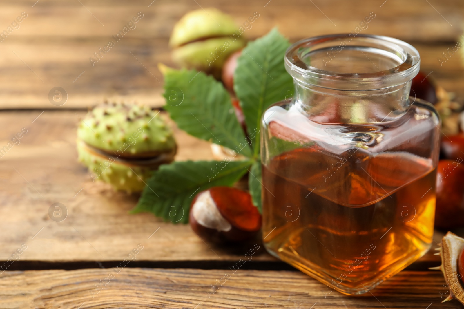 Photo of Chestnuts and jar of essential oil on wooden table. Space for text