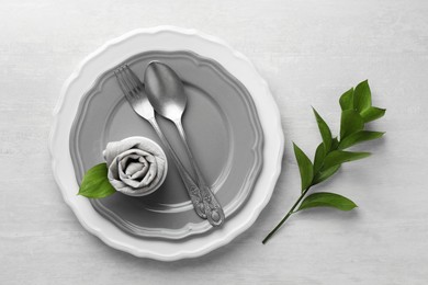 Stylish setting with cutlery, napkin, branch and plates on light textured table, top view. Space for text