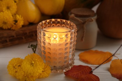 Photo of Burning candle, chrysanthemums and yellow leaves on white wooden table