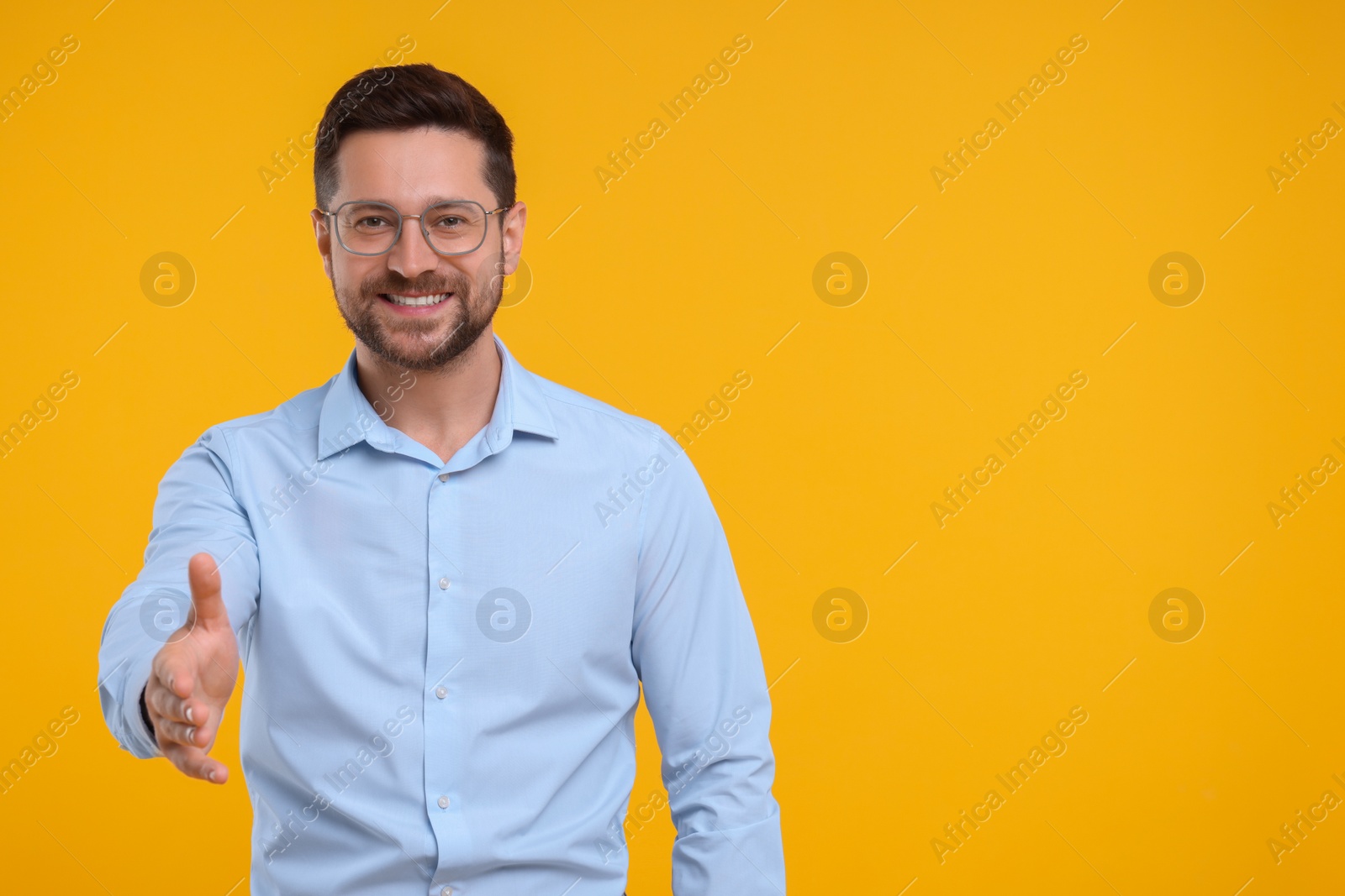 Photo of Happy man welcoming and offering handshake on yellow background. Space for text