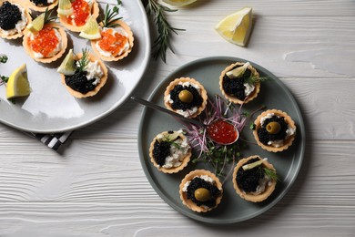 Delicious tartlets with red and black caviar served on white wooden table, flat lay