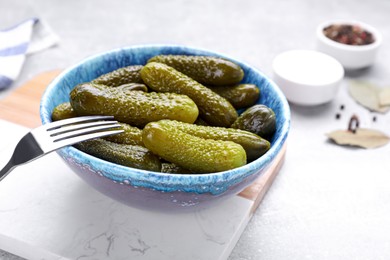 Photo of Fork with bowl of pickled cucumbers on light grey table, closeup