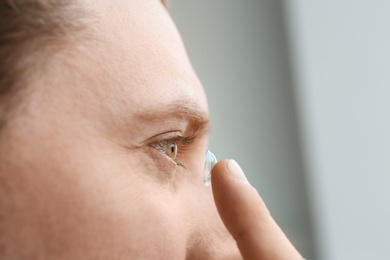Photo of Young man putting contact lens in his eye on light background, closeup