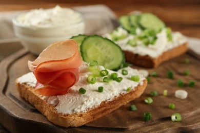 Delicious sandwiches with cream cheese and other ingredients on wooden board, closeup