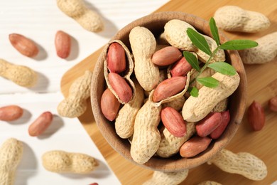 Fresh unpeeled peanuts in bowl and twig on white table, top view