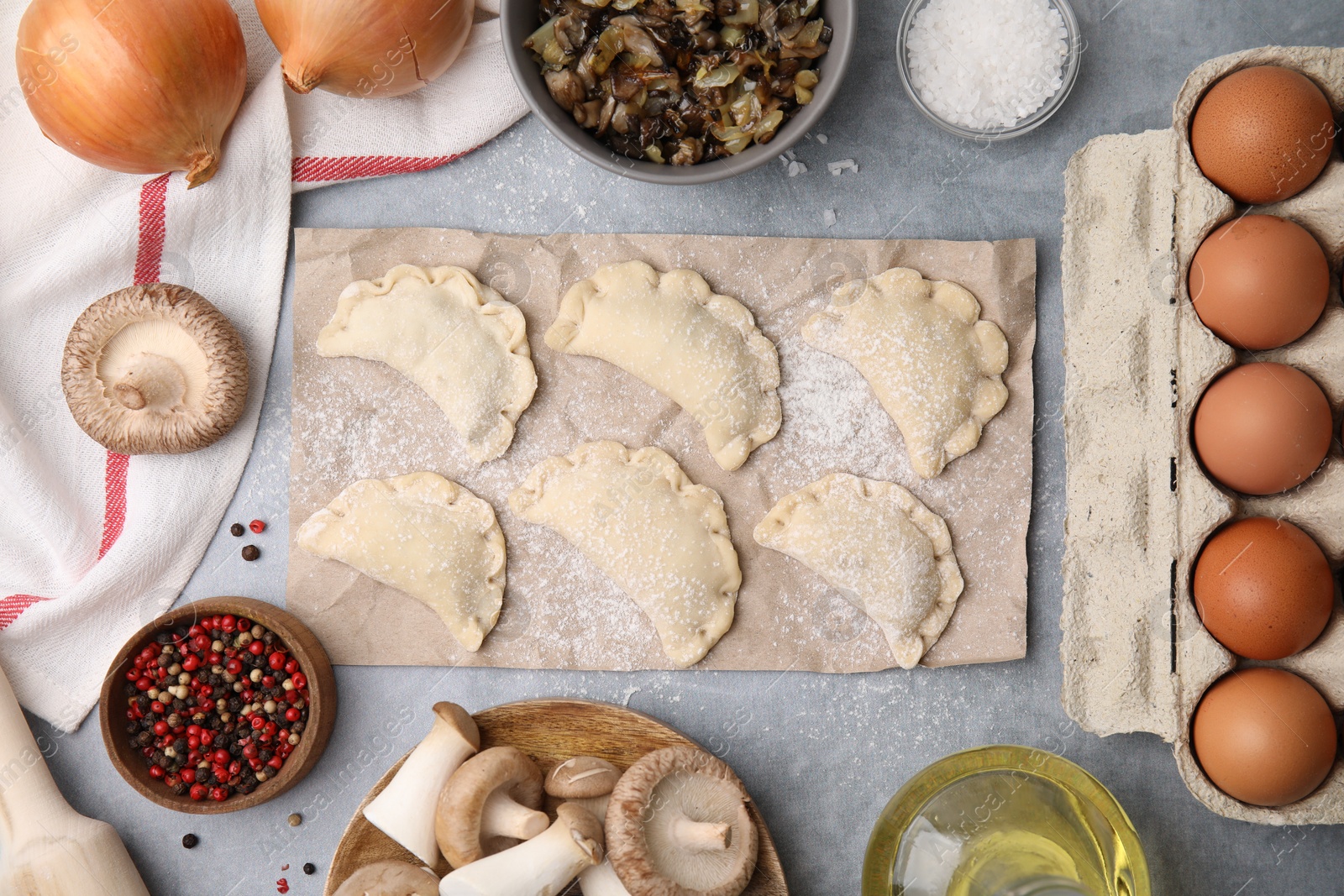 Photo of Process of making dumplings (varenyky) with mushrooms. Raw dough and ingredients on grey table, flat lay