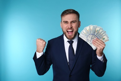 Portrait of emotional young businessman with money on color background