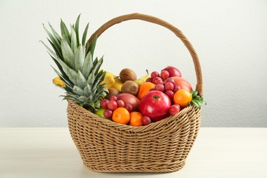 Wicker basket with different fresh fruits on white wooden table