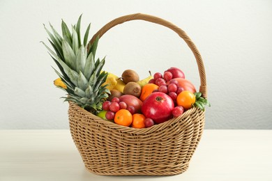 Photo of Wicker basket with different fresh fruits on white wooden table