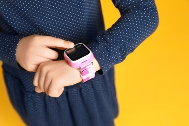 Photo of Little girl with smart watch on yellow background, closeup