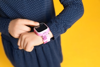 Little girl with smart watch on yellow background, closeup