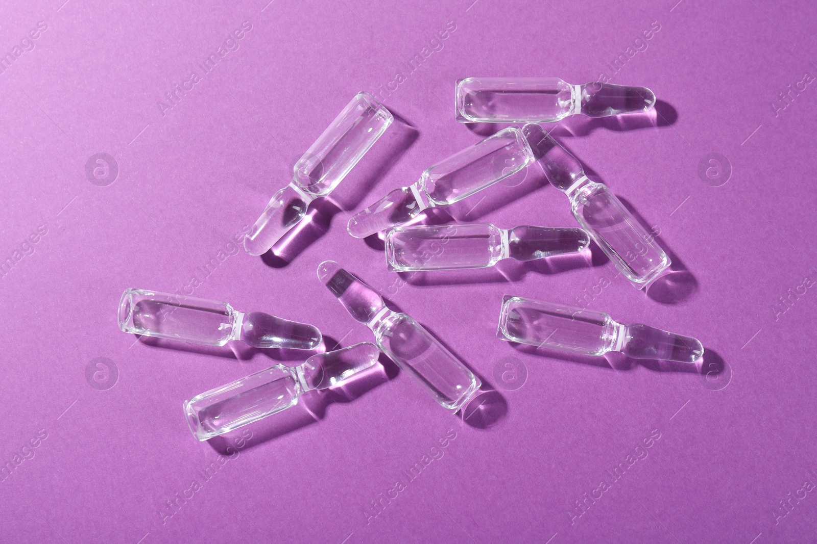 Photo of Glass ampoules with liquid on purple background, top view