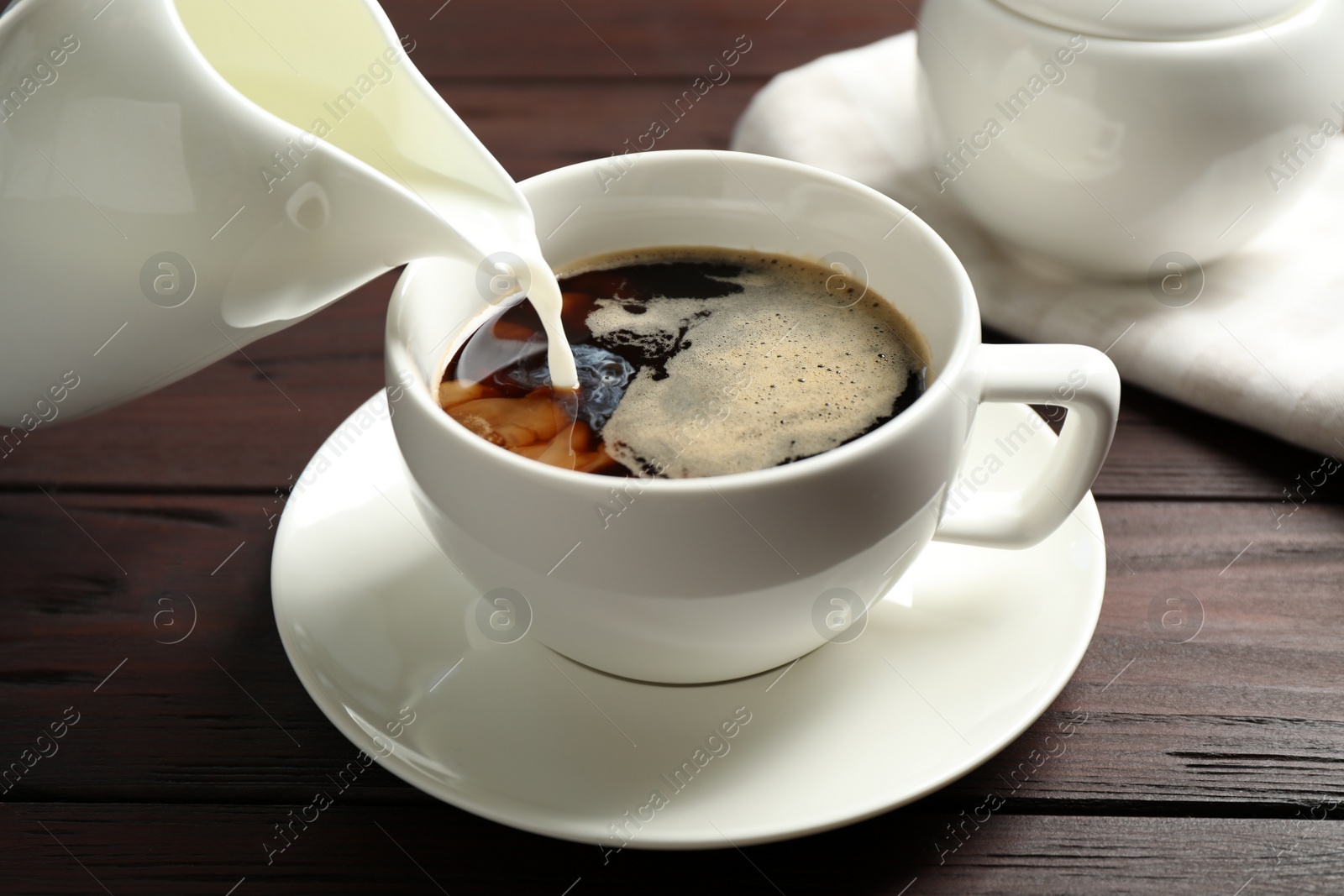 Photo of Pouring milk into cup of hot coffee on wooden table