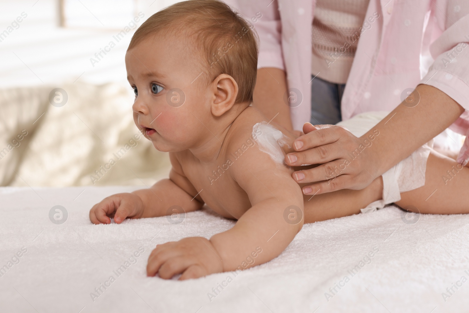 Photo of Mother applying body cream on her little baby at home, closeup