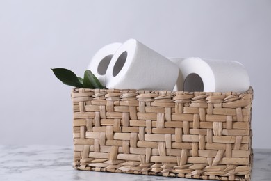 Photo of Toilet paper rolls and green leaves in wicker basket on white marble table